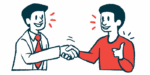 A doctor shakes hands with a patient who is making a thumbs-up gesture.
